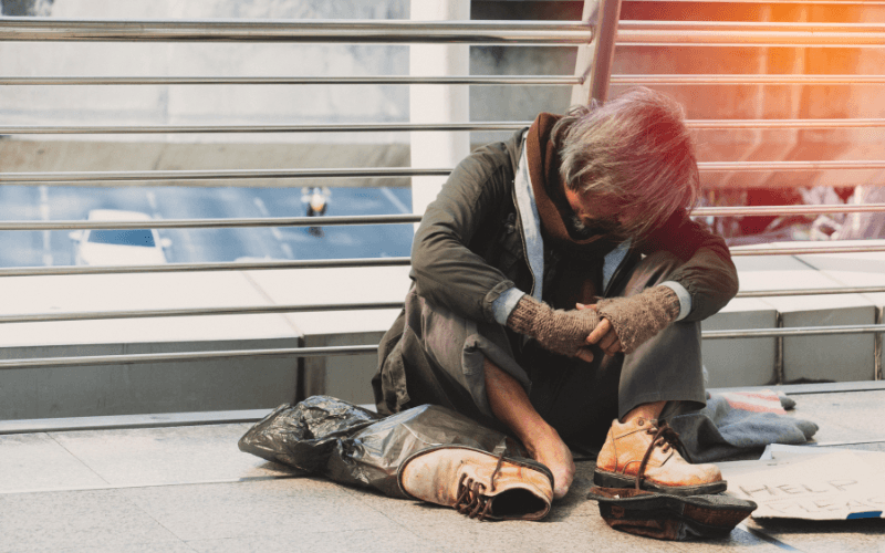A homeless person sitting on a street, representing the struggles of the poor in Islam and beyond.
